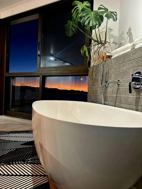 Bathroom with a freestanding tub and a window showing dusk light over distant hills