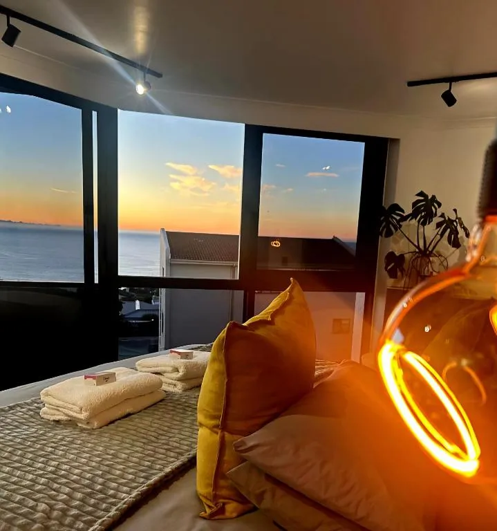 Bedroom with a sea-view window at sunset, folded towels on the bed, and a decorative glass lamp