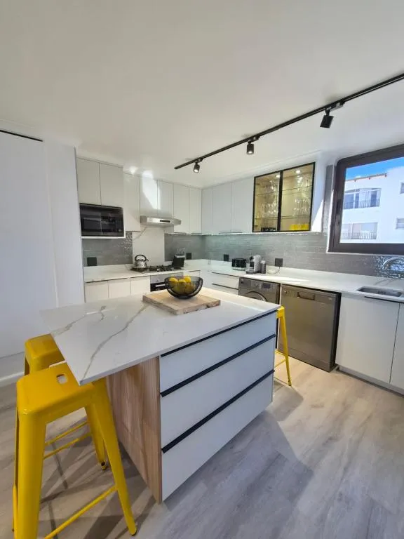 Kitchen with white cabinetry, yellow bar stools, and a window onto the neighbouring building