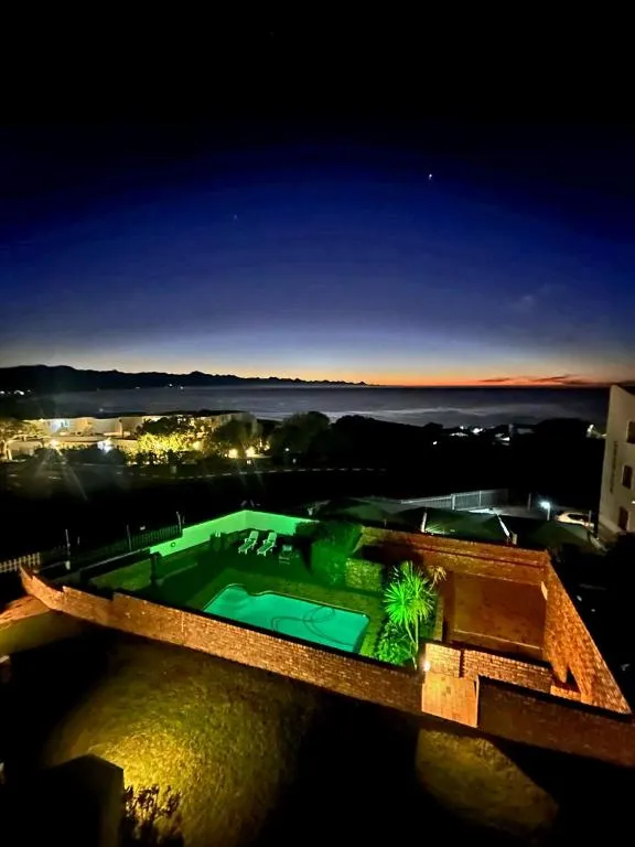 Night view from the balcony over a lit communal pool with the coastline beyond