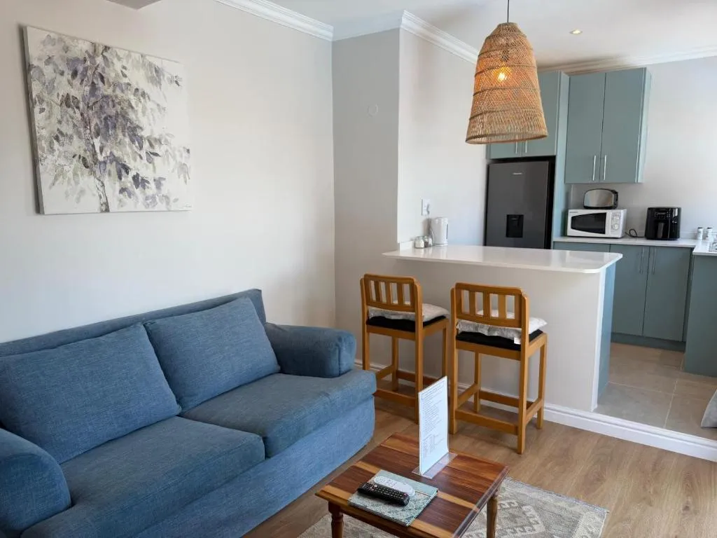 Open-plan lounge, dining bar and kitchen with pale blue cabinetry under a woven pendant light