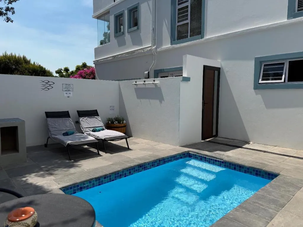 Small tiled plunge pool and two loungers in a walled courtyard below blue-trimmed windows