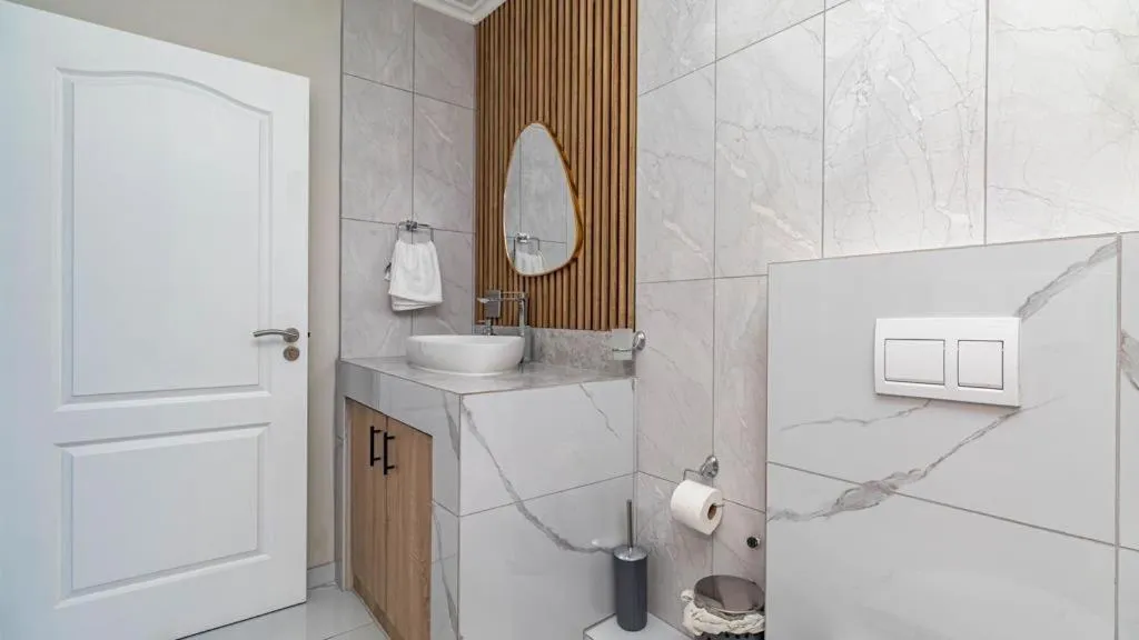 Bathroom with marble-tiled vanity, oval mirror and wall-hung toilet
