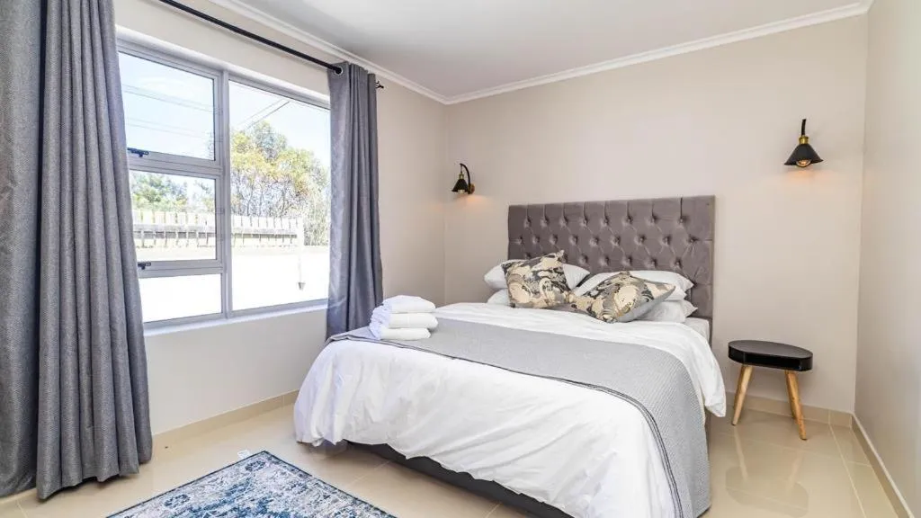 Bedroom with upholstered grey headboard, bedside sconces and a curtained window