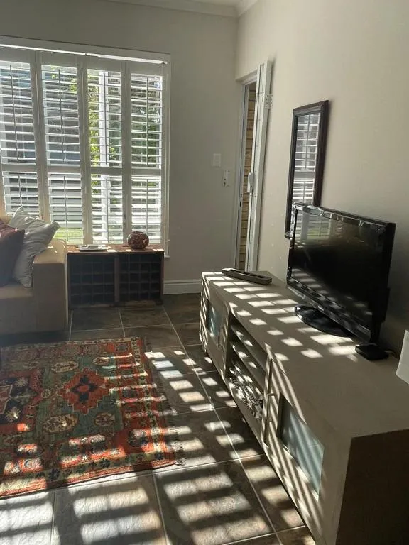 Second living space with a wall-mounted TV, patterned rug and shuttered window
