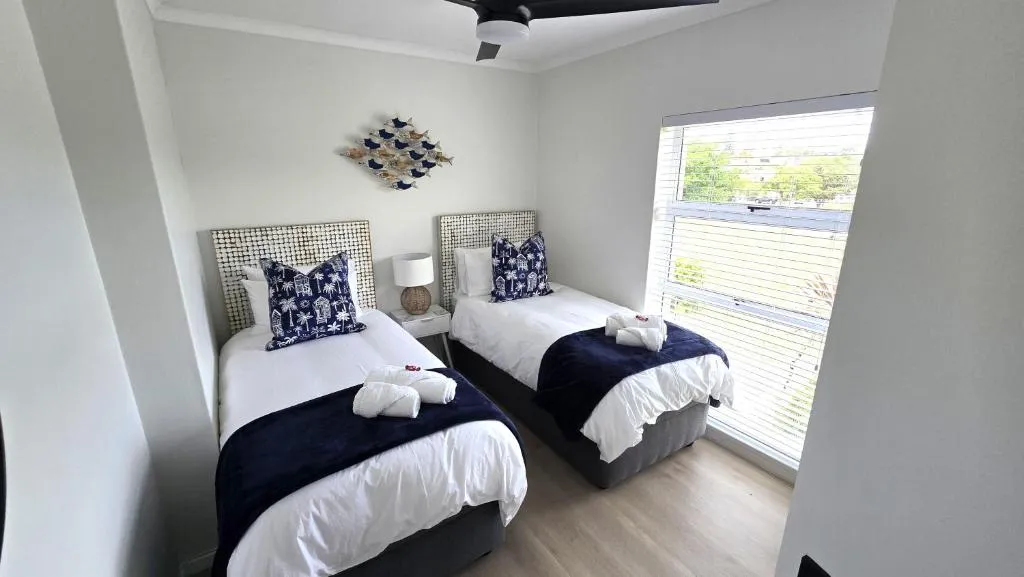 Twin bedroom with woven headboards, navy accents and a window overlooking the garden