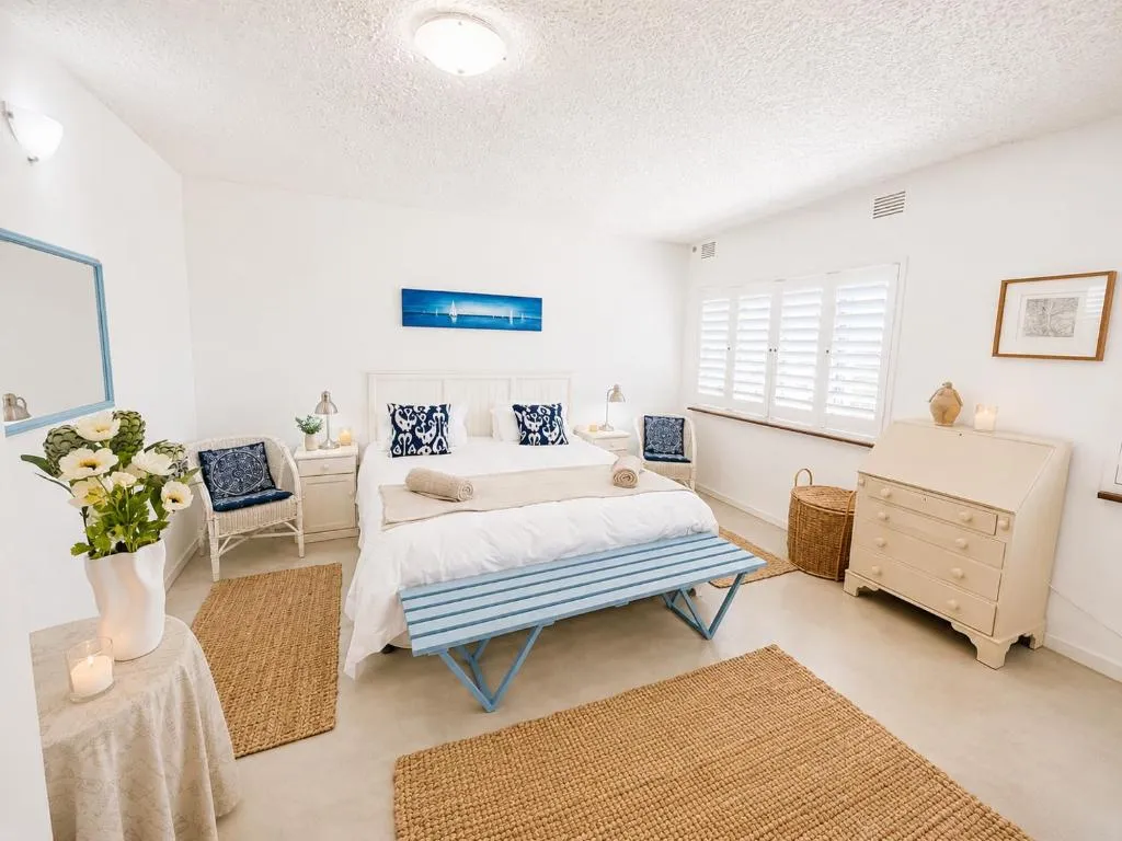 Bedroom with a nautical sailboat print and a blue-striped bench at the foot of the bed