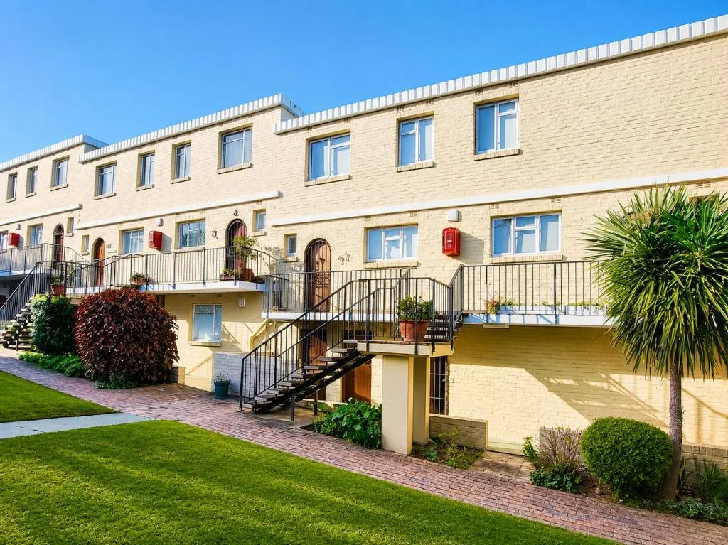 Yellow-brick apartment block with external staircases and a landscaped garden strip