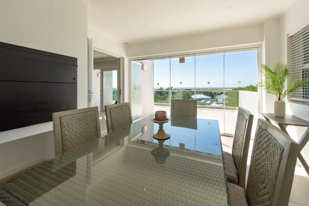 Dining area with glass doors open to a tiled balcony overlooking the coastline