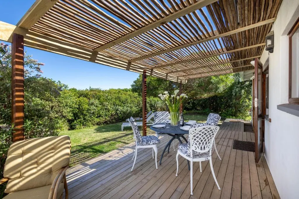 Pergola-covered outdoor dining table set on a deck opening onto the garden