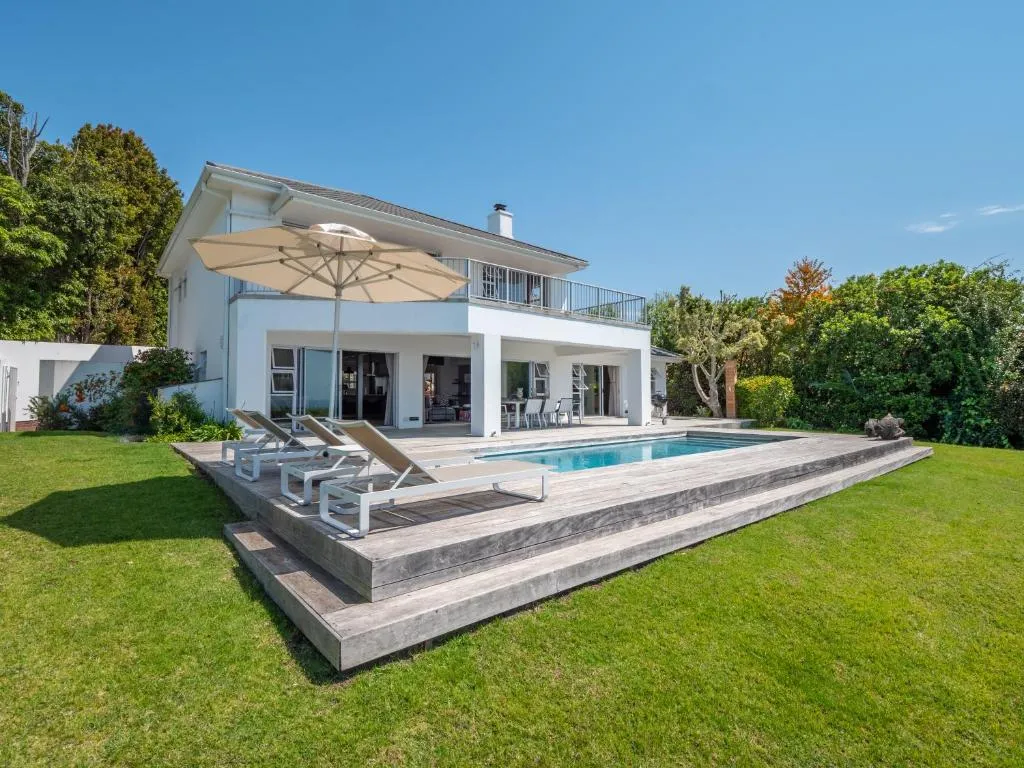 Double-storey house with a raised timber-deck pool, loungers and lawned garden
