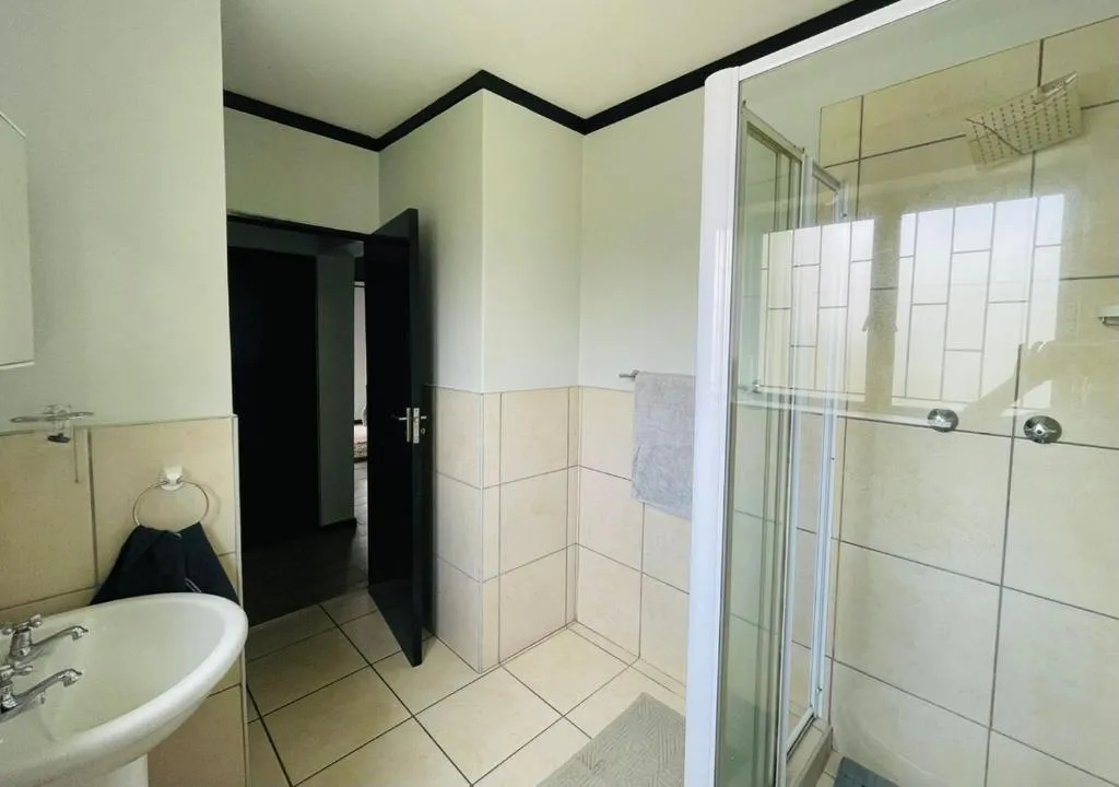 Bathroom with a pedestal sink, tiled shower stall and a hallway view beyond