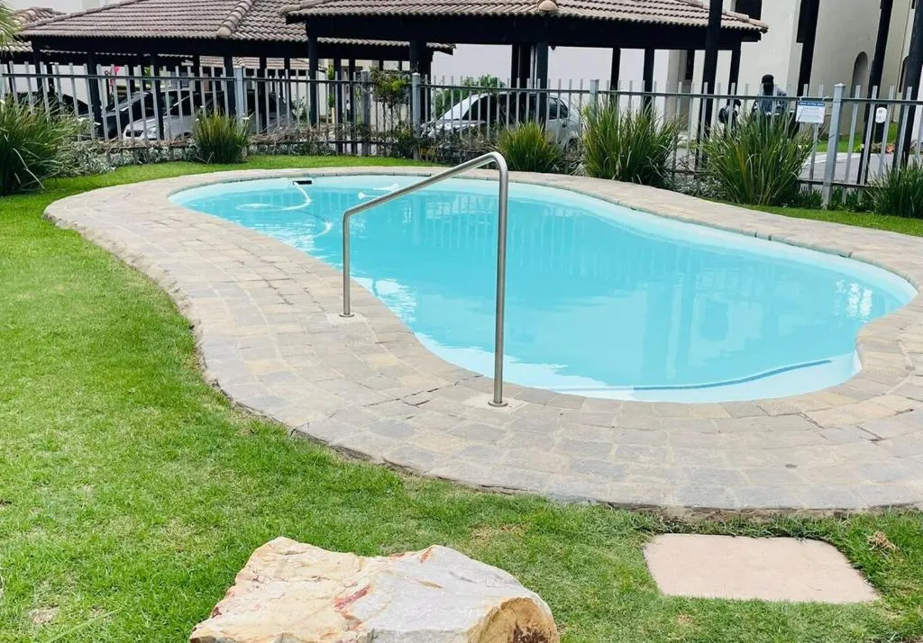 Communal kidney-shaped pool in the complex's fenced garden near the carport