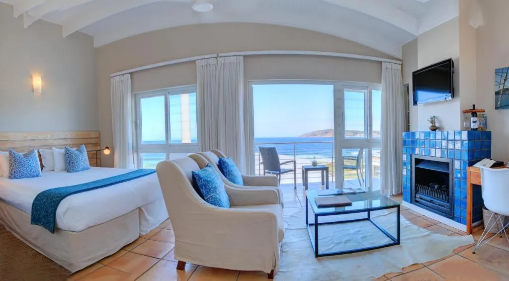 Sea-view suite with a blue-tiled fireplace, upholstered armchairs and a private balcony over the beach