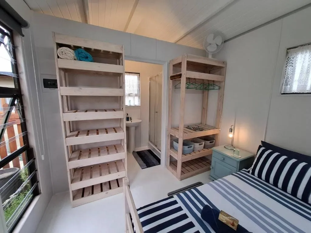 Bedroom with open timber shelving for storage and a striped bed against the window