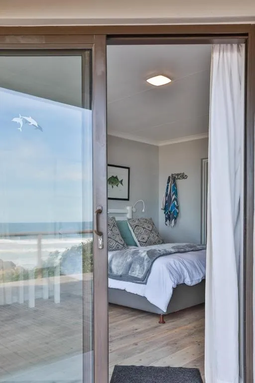 Bedroom seen through a sliding glass door onto a deck with a clear view of the beach and sea