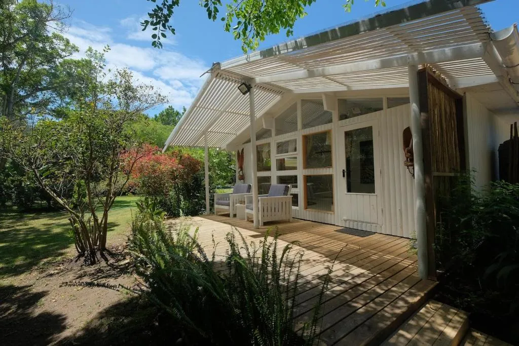 Cottage exterior with a pergola-covered timber deck, lounge chairs, and a garden setting