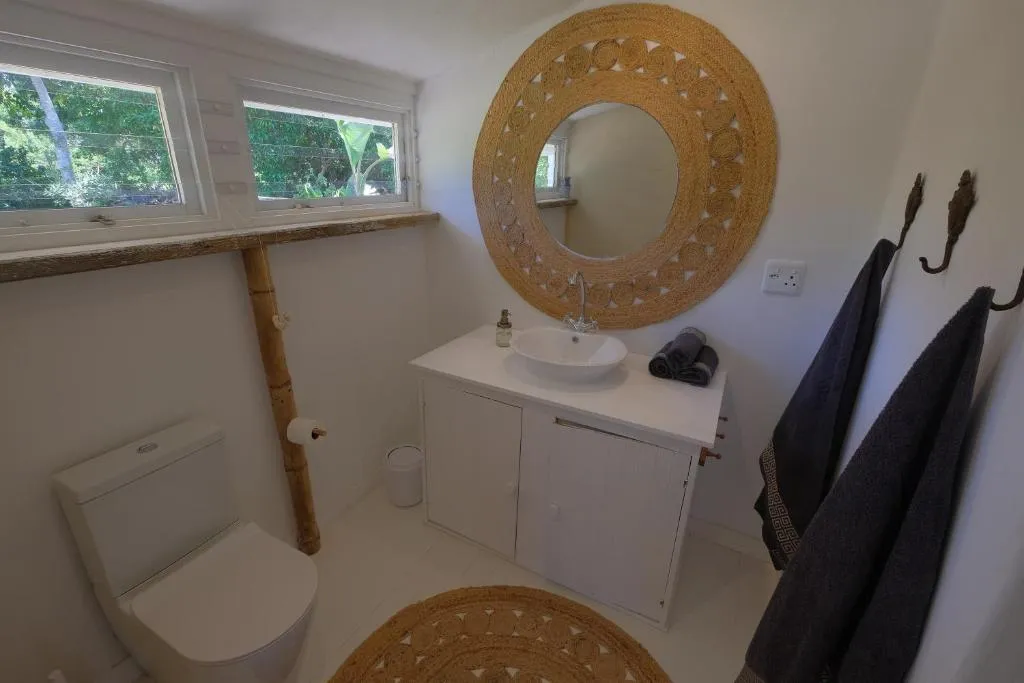 Bathroom with a round woven-frame mirror, vessel basin and bamboo towel rail beneath a window