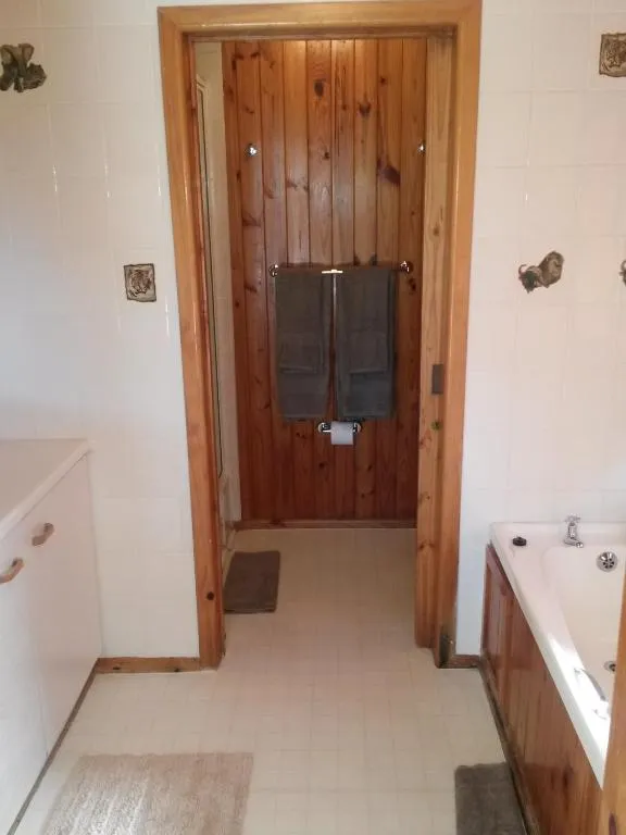 Bathroom passage with a towel rail and a built-in corner tub beside a pine door