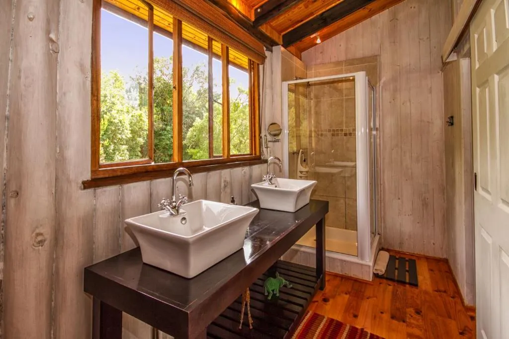Bathroom with twin vessel sinks on a dark timber vanity below a window onto the forest