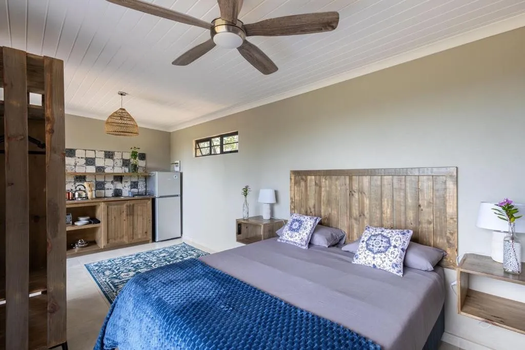 Open-plan studio bedroom with kitchenette, wood headboard and ceiling fan