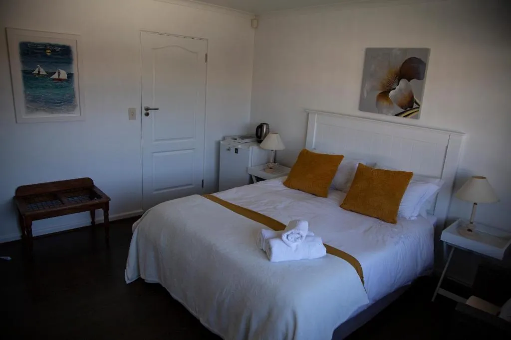 Bedroom with a white bedspread, mustard cushions and a framed sailboat painting above a wood bench