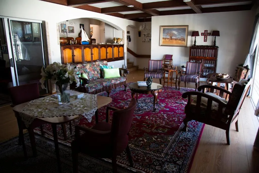 Living and dining area with a dark wood beamed ceiling, floral sofa and patterned burgundy rug