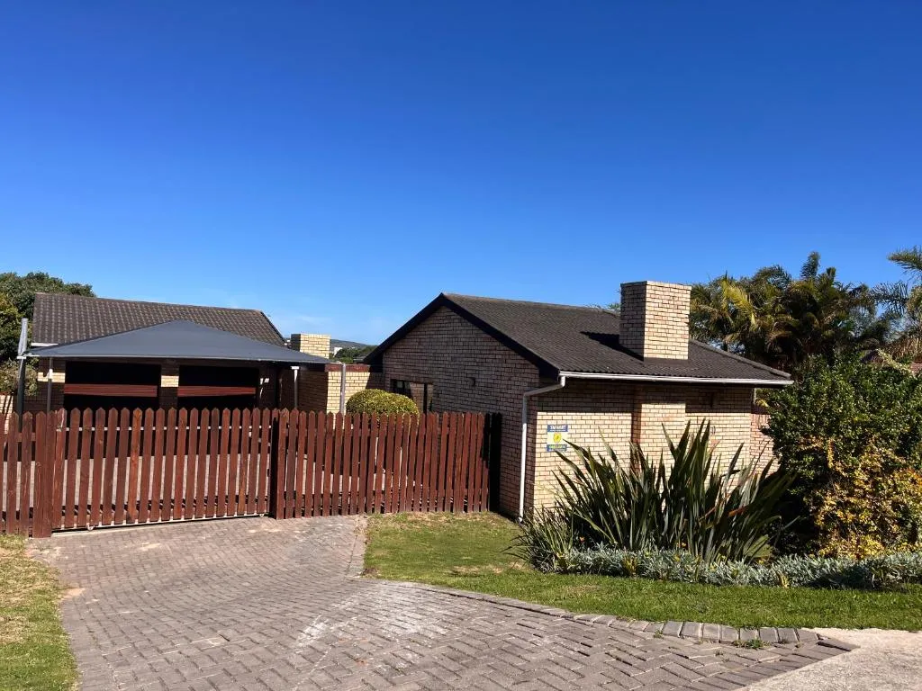 Single-story brick holiday home behind a dark wooden picket fence and paved driveway