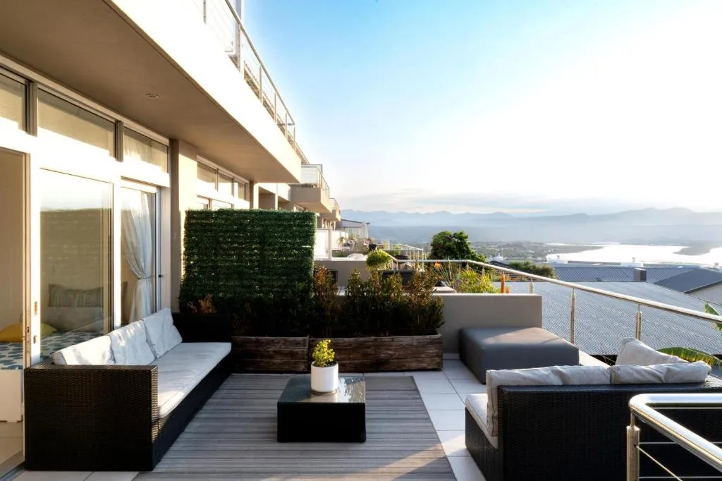 Furnished balcony behind a privacy hedge with views over rooftops to distant mountains and the lagoon