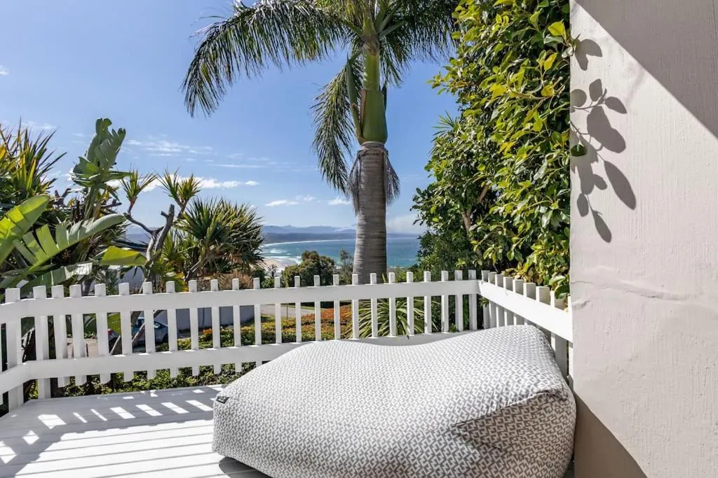 Covered balcony with a cushioned daybed and palm trees framing a sea and mountain view