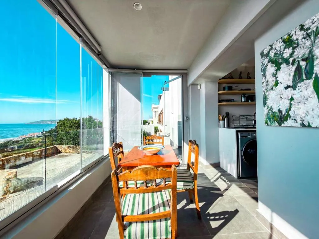 Wooden dining table for four in a glassed sunroom looking out to the ocean