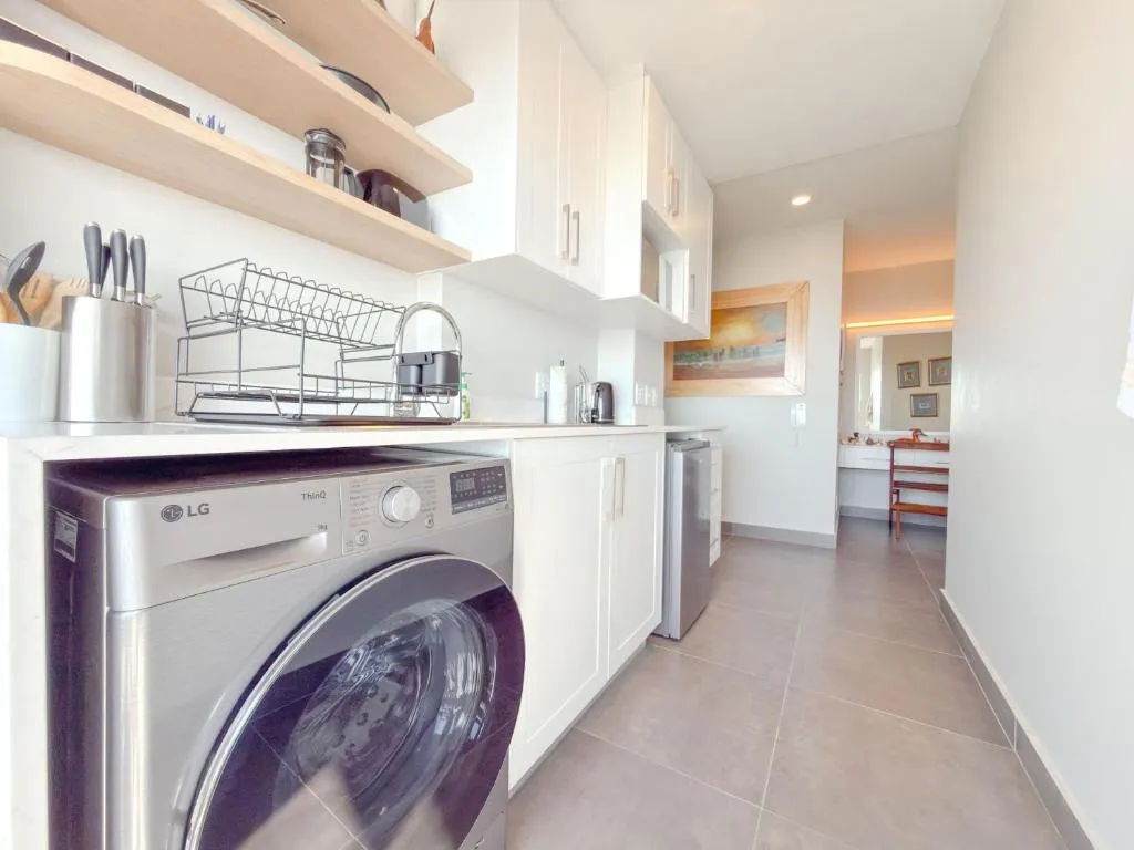 Galley kitchen with front-loader washer, open shelving and white cabinetry
