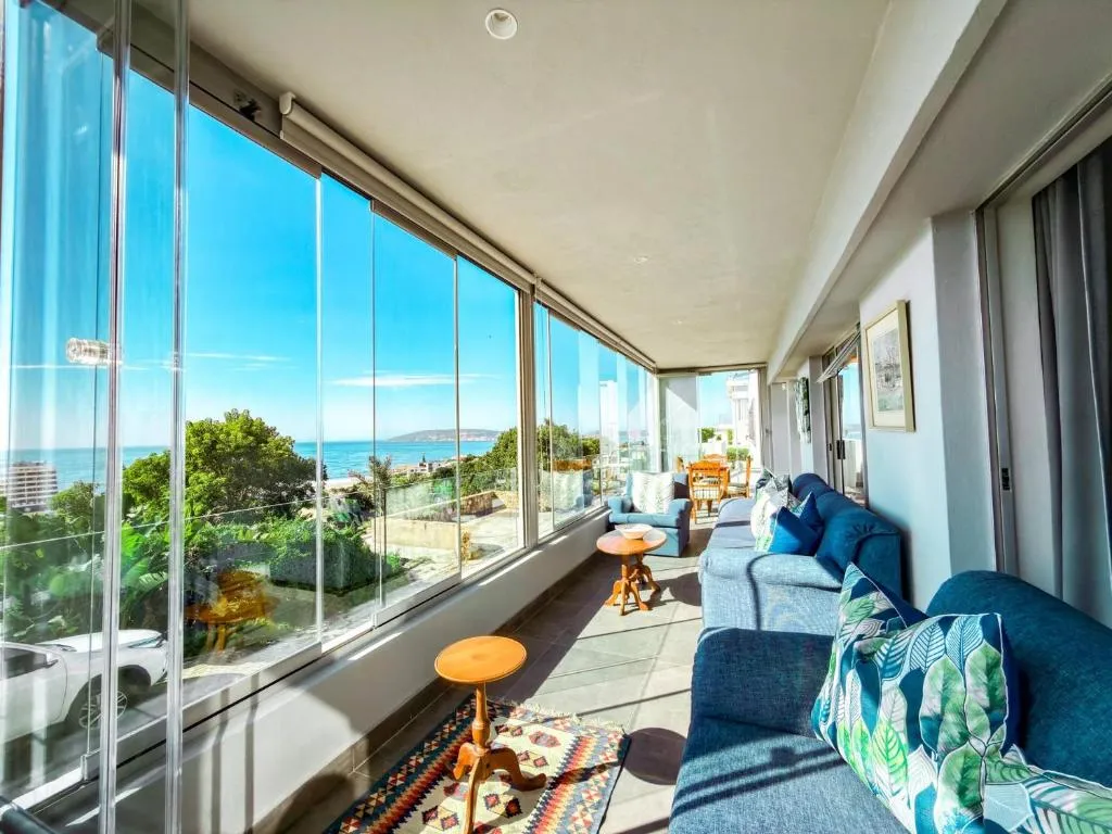 Glassed sunroom lounge with blue sofas and a wide-angle view over the bay