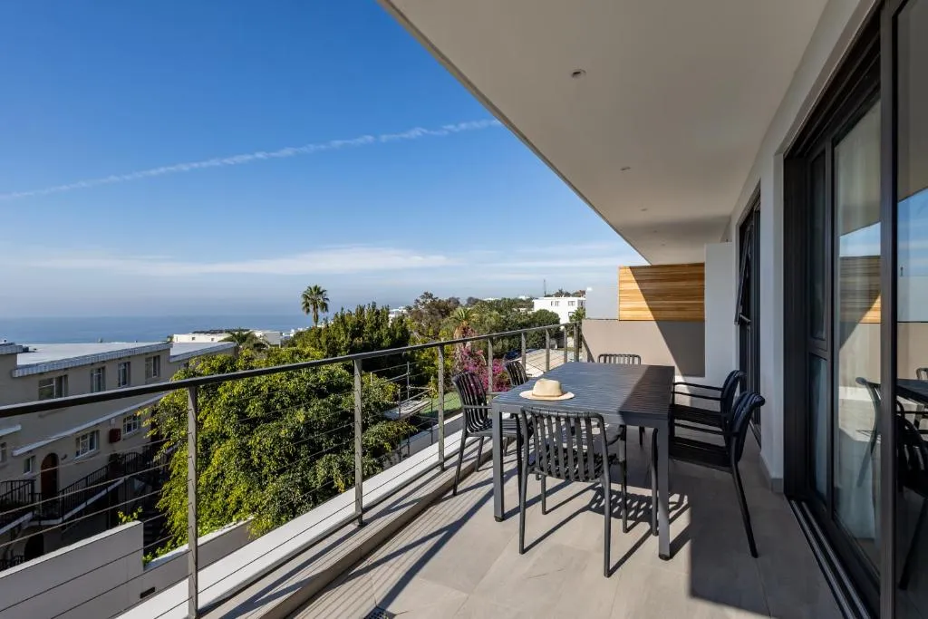 Balcony dining table with a sun hat resting on it, overlooking the coastline and rooftops