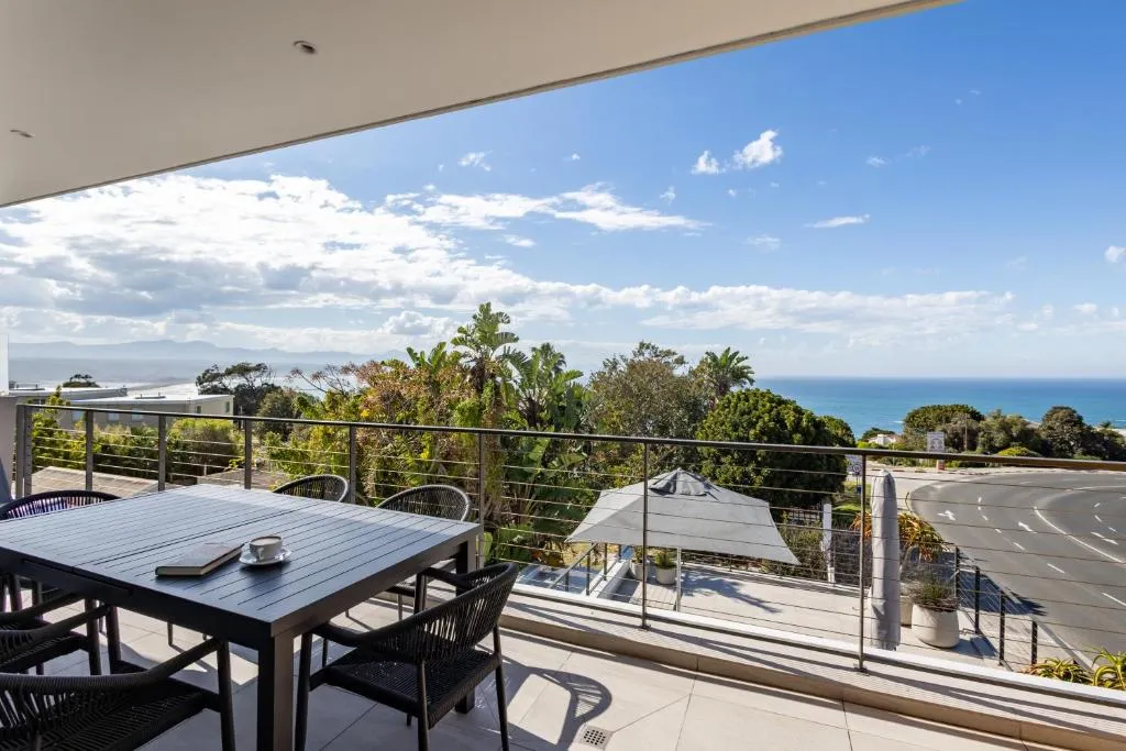 Balcony dining table facing the ocean and a curving coastal road below