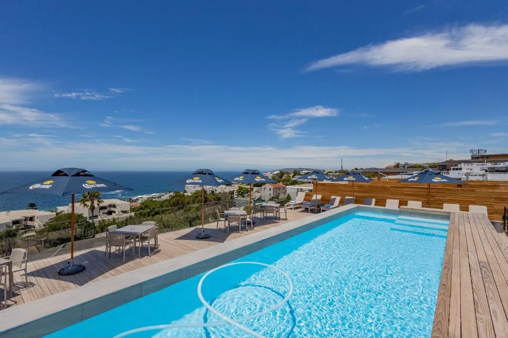 Rooftop pool deck with dining tables under umbrellas and a panoramic sea view