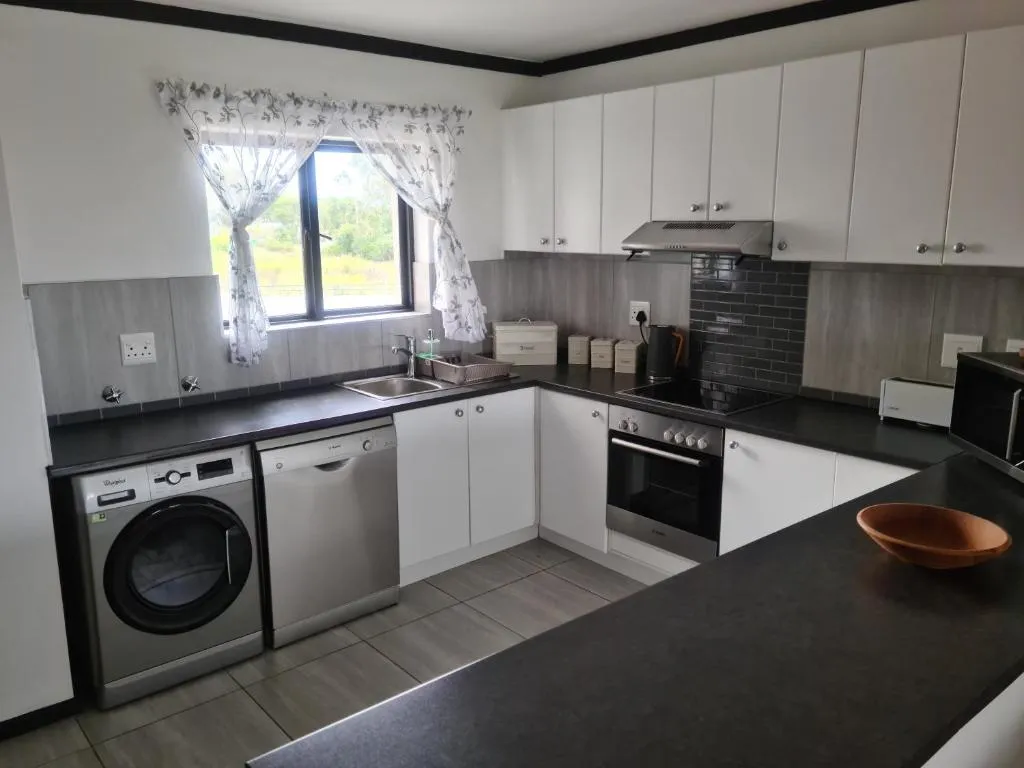 Kitchen with a washing machine, dishwasher and a window looking out over open green parkland