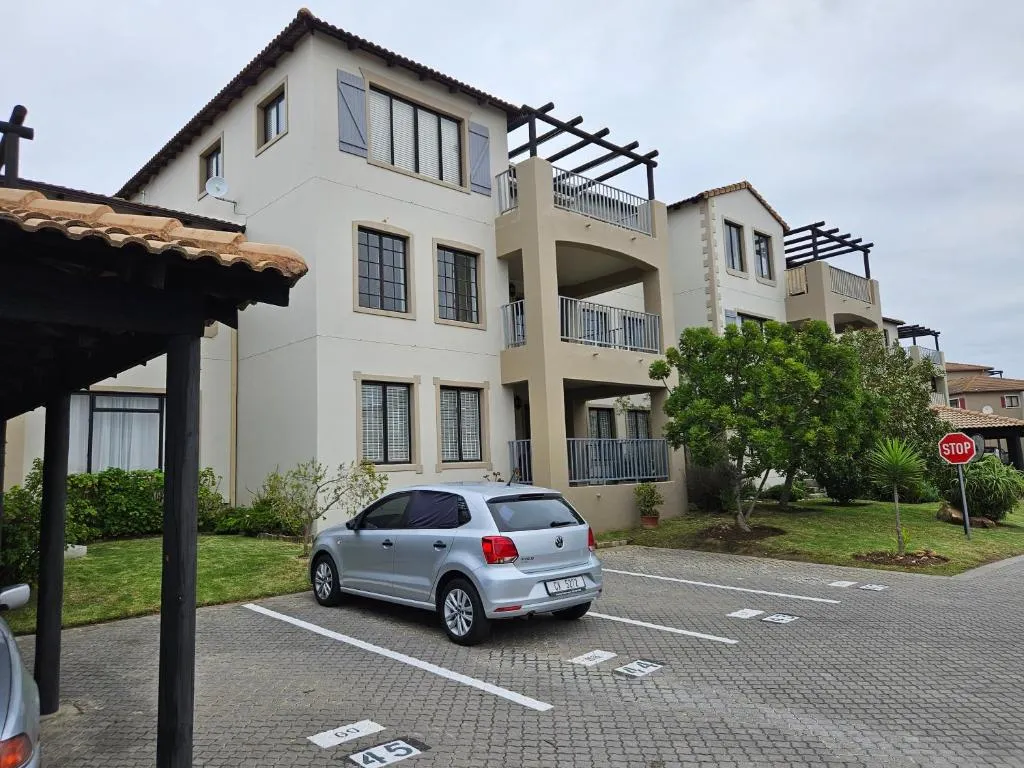 Three-storey apartment building exterior with balconies, parking bays and a paved driveway