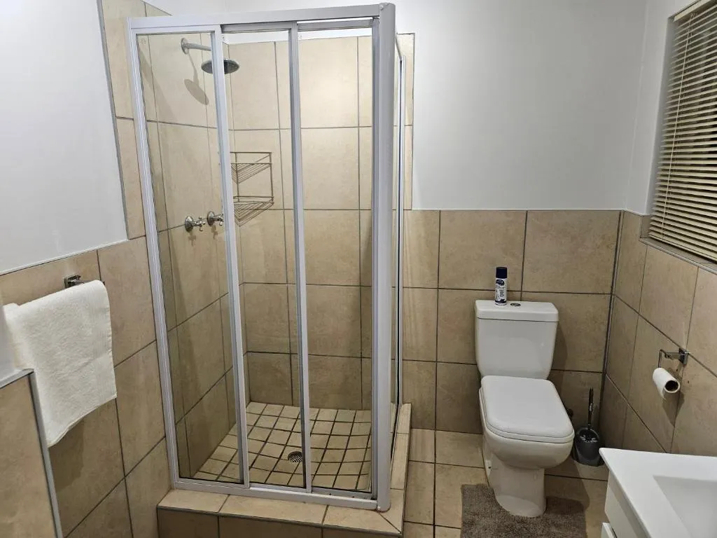 Shower bathroom with a glass-enclosed cubicle, toilet and tiled walls