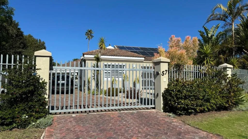 Solar-paneled home behind a wrought-iron gate with palms and a paved driveway