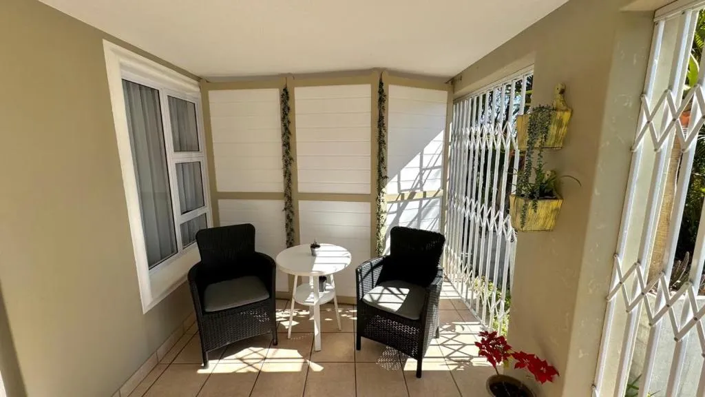 Small tiled porch with two wicker armchairs and a side table beside a barred window