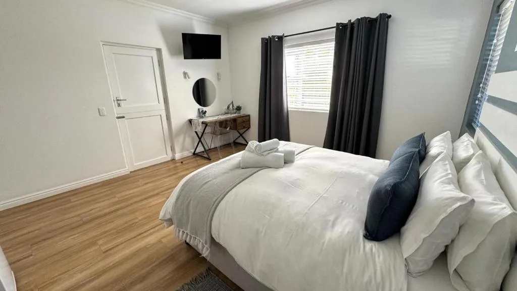 Second bedroom with a wall-mounted TV, a round mirror over a writing desk and dark curtains