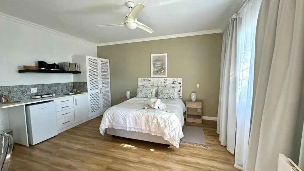 Self-catering studio with kitchenette, queen bed and ceiling fan on wood-look flooring