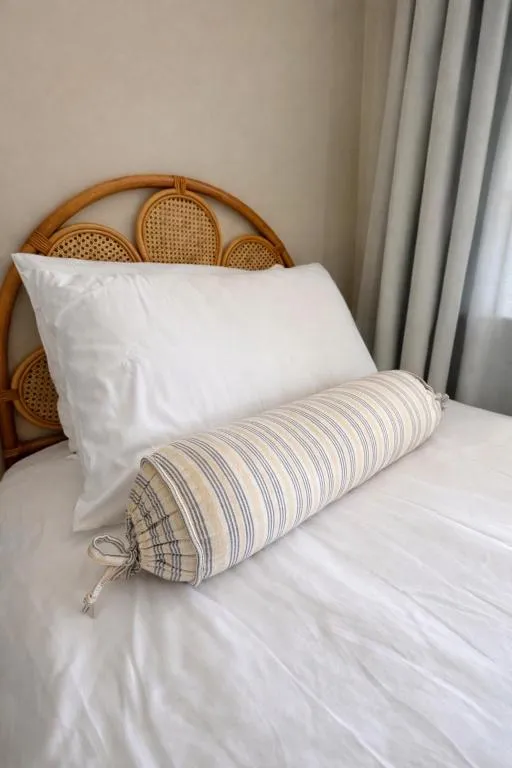 Close-up of the rattan cane headboard with white pillows and a striped bolster
