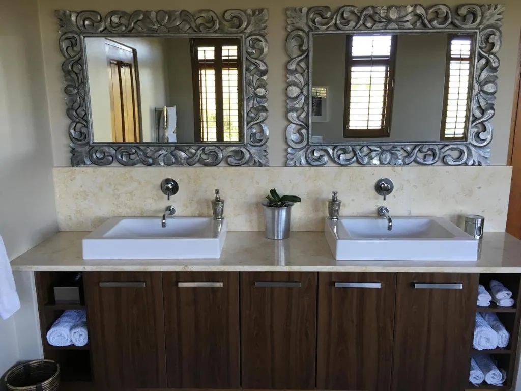 Bathroom with twin vessel sinks, ornate carved mirrors and dark wood cabinetry