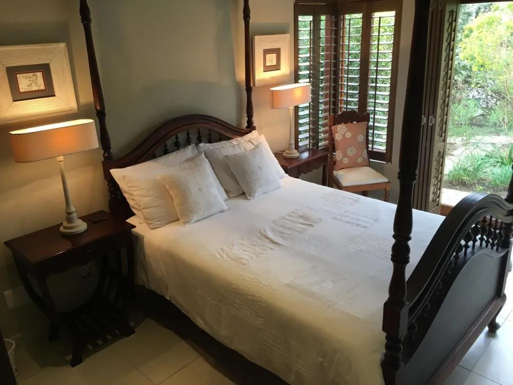 Bedroom with a dark wood four-poster bed and plantation shutters opening to the garden