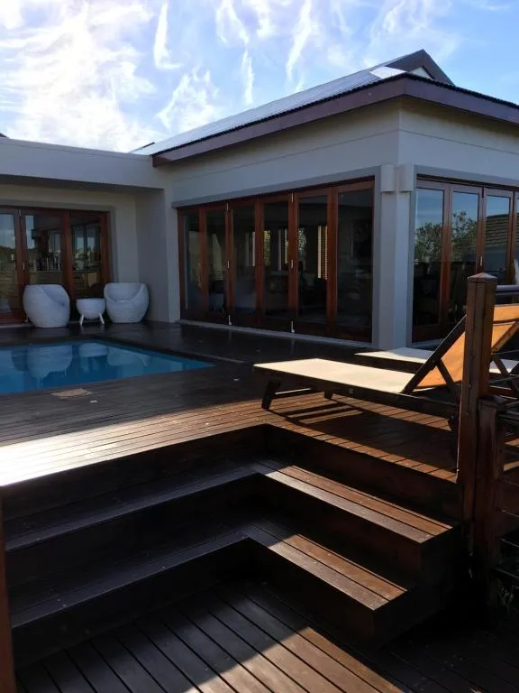 Pool and folding-door house exterior with white pod chairs on a wooden deck