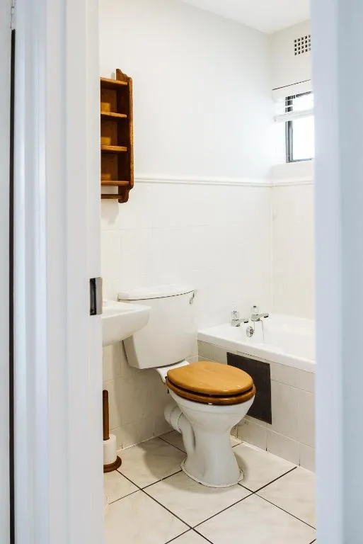 Bathroom with a wood-seat toilet, corner bathtub and wall shelving, viewed through the open door