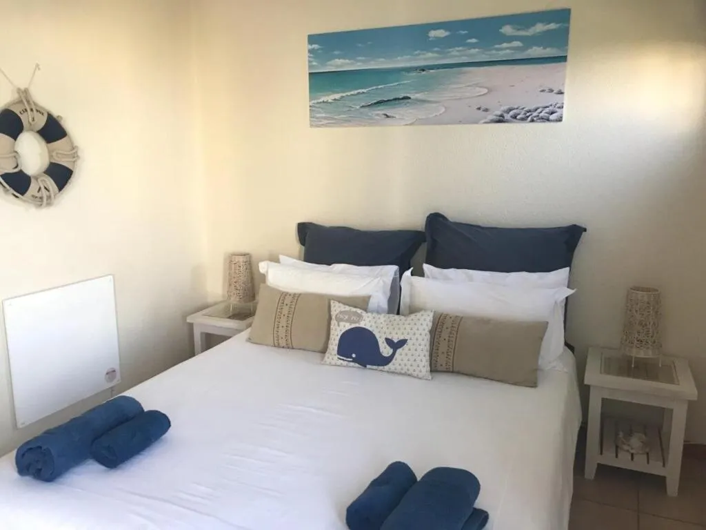 Bedroom with nautical decor, navy pillows, a life-buoy wall hanging and rolled blue towels on white linen