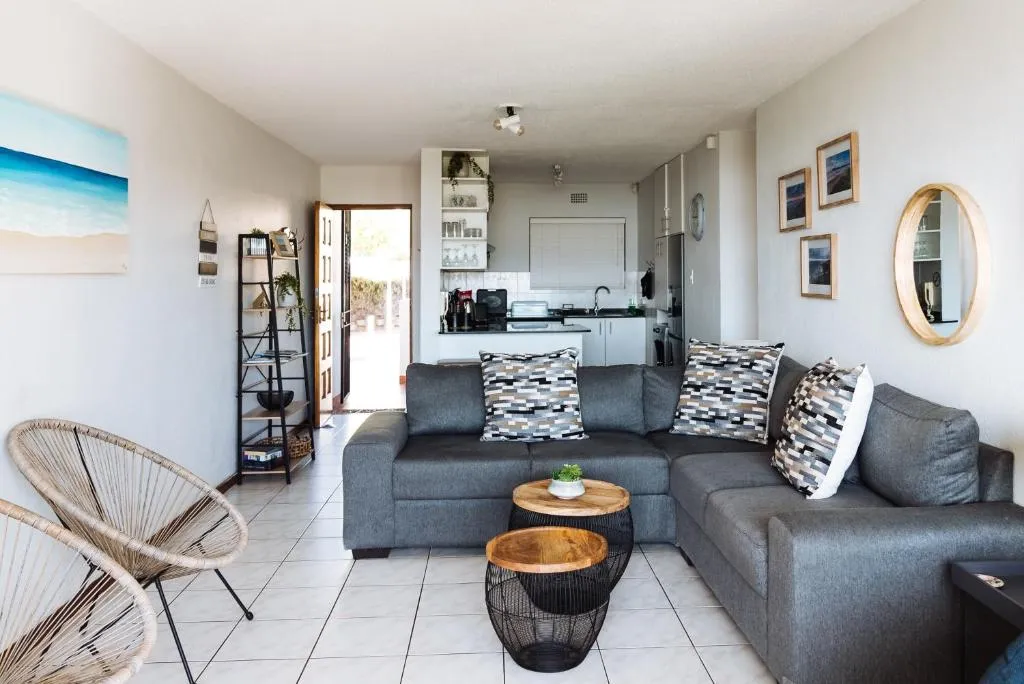 Open-plan living area with a grey corner sofa, wicker chairs and a view through to the kitchen